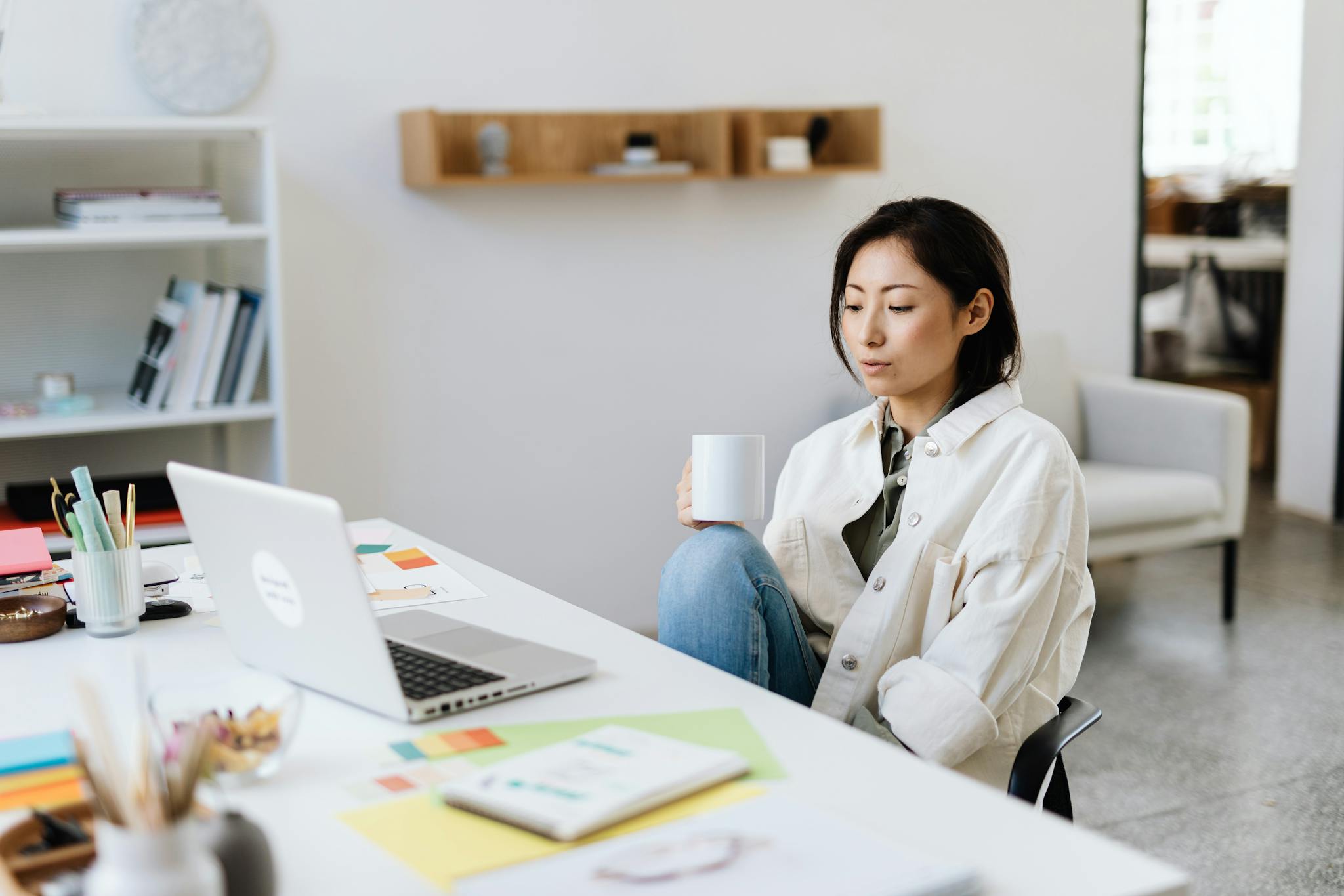 Businesswoman in a modern office setting working on a laptop with a coffee cup.